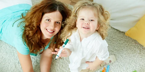 Babá sorrindo deitada no tapete brincando com uma criança pequena