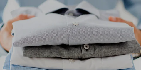 Mãos segurando camisas sociais passadas e dobradas cuidadosamente
